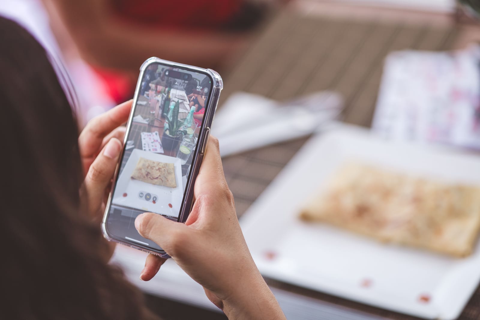 Person photographing a plated dish on a restaurant table with a phone