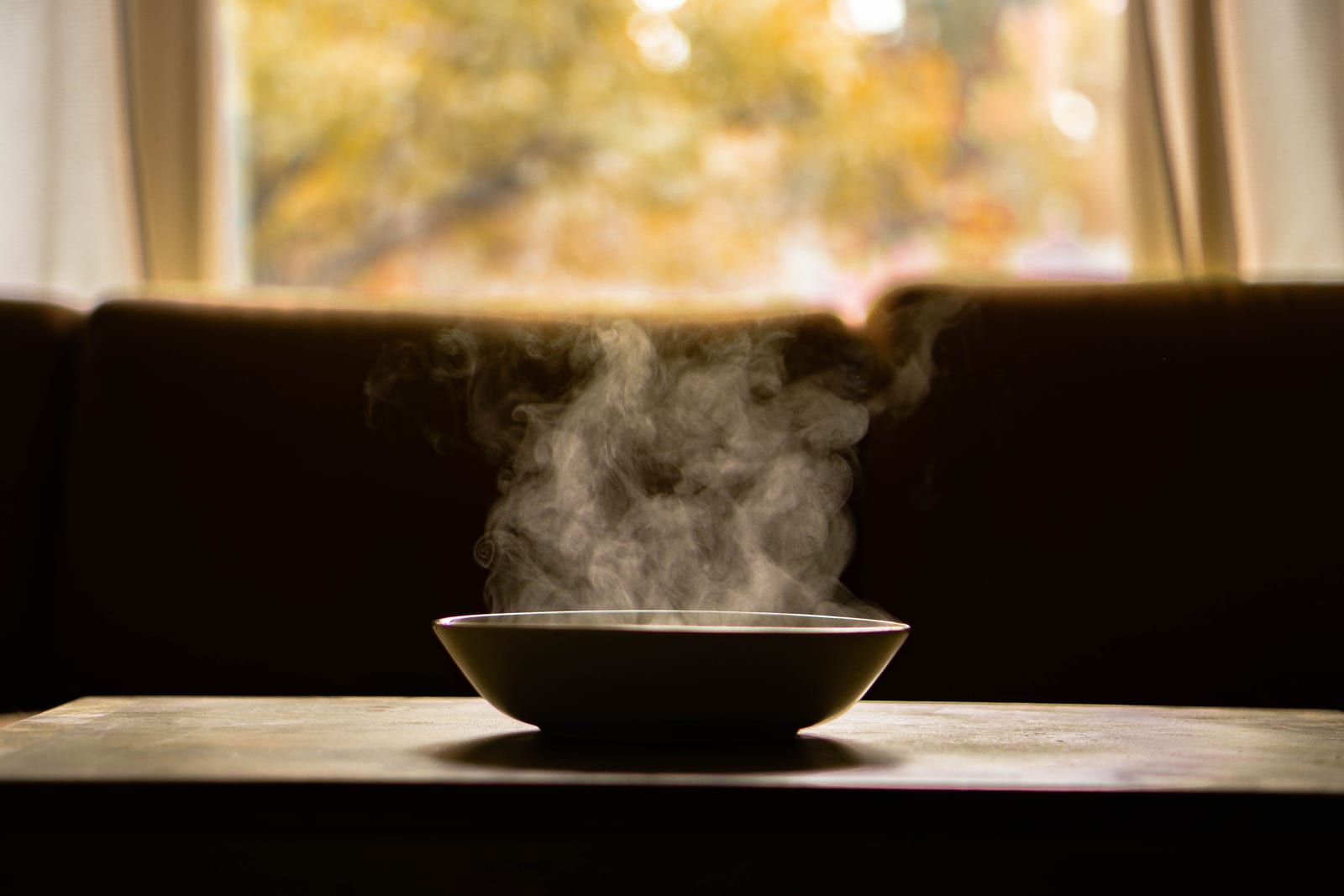 Close-up of a steaming bowl of soup on a wooden table with soft backlight